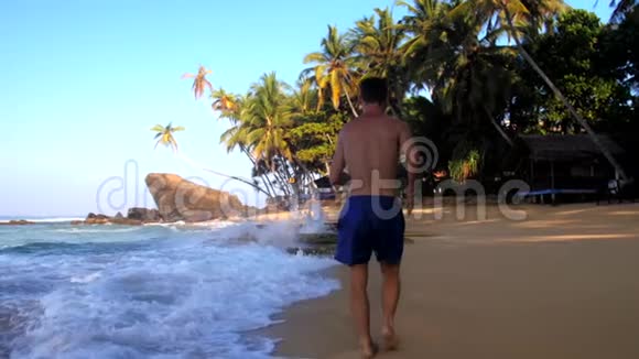 盖伊沿着沙滩上起伏的海浪奔跑视频的预览图