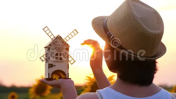 一个戴草帽的女孩站在向日葵的田野里手里拿着一个玩具磨坊对着夕阳视频的预览图