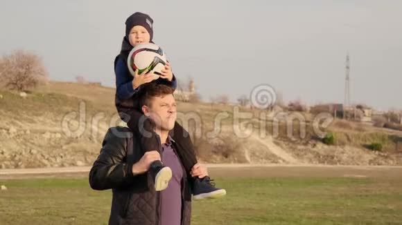 爸爸和他的小儿子一起在户外慢动作踢足球时肩膀上跳视频的预览图