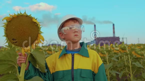 幼儿戴着防护面罩与背景工业厂房上的植物向日葵环境污染视频的预览图