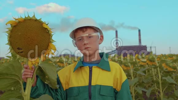 幼儿戴着防护面罩与背景工业厂房上的植物向日葵环境污染视频的预览图
