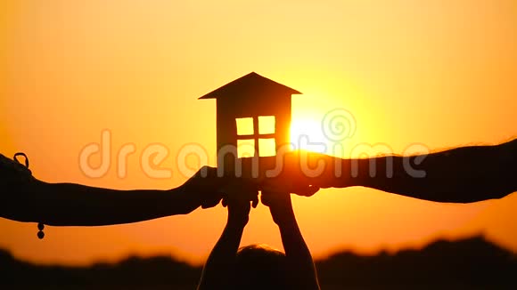 一个幸福的家庭在美丽的日落背景上保留了一个纸房子家庭关系爱情的概念视频的预览图
