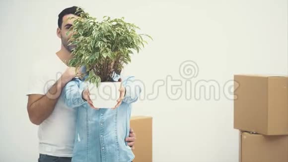 年轻夫妇一起搬到了一间新公寓他们拿着一个绿色的花盆微笑着动作动画4K视频的预览图