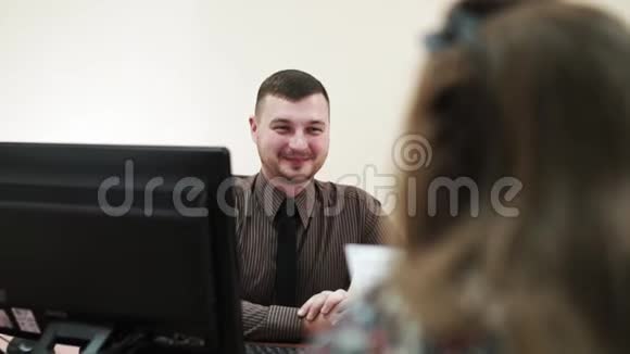 年轻的商人坐在办公室的办公桌前微笑着看着一位女员工视频的预览图