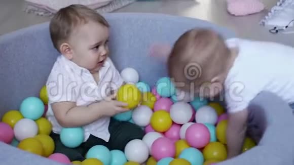 婴儿从另一个坐在球池里的小男孩手中捡起一个塑料球视频的预览图