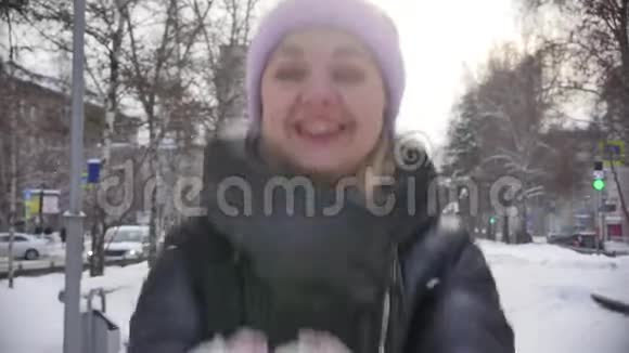 一个穿着粉红色帽子的开朗可爱的年轻女人扔了第一场雪嘲笑相机概念寒假视频的预览图