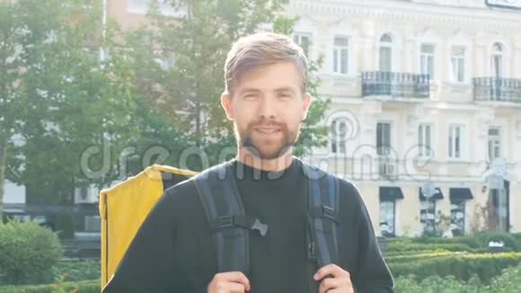 城市里一个带着黄色袋子的微笑的年轻快递员的肖像黎明时带背包的长胡子家伙交货视频的预览图