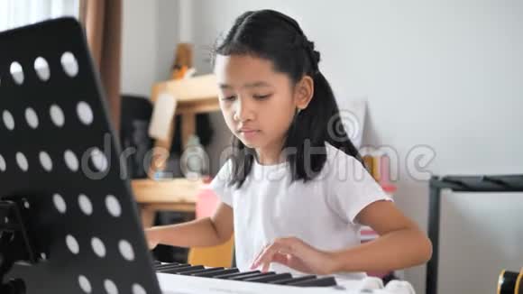 亚洲小女孩通过使用电合成器键盘学习基本钢琴用于初学者音乐器乐自学视频的预览图