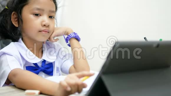 穿着泰国小学制服的亚洲小女孩用平板智能手机做作业用于技术和教育视频的预览图