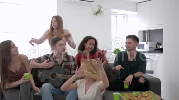 一群无忧无虑的朋友在家里开派对年轻人正玩得很开心坐在沙发上弹着吉他唱歌视频的预览图