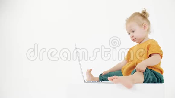 严肃的女婴看着白色背景的笔记本电脑屏幕视频的预览图