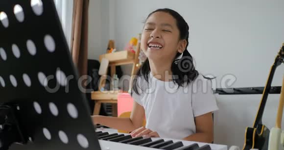 亚洲小女孩通过使用电合成器键盘学习基本钢琴用于初学者音乐器乐自学视频的预览图