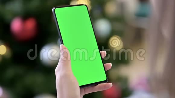 圣诞树附近的女性手持Chroma键屏智能手机视频的预览图