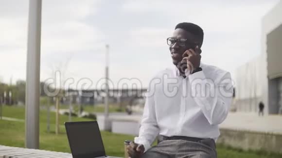 年轻的非洲商人带着眼镜在城市公园里打电话喝咖啡视频的预览图