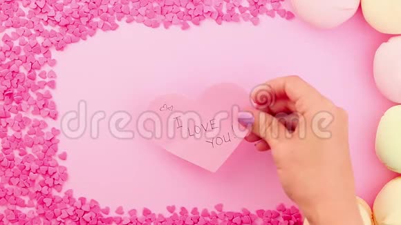 女人用手放一张情人节卡片我爱你在粉红色的背景上签名视频的预览图