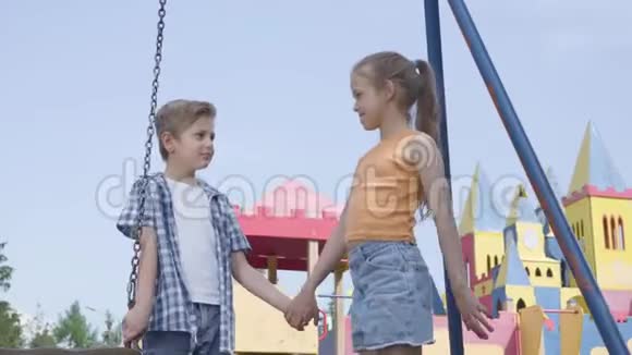 小男孩和美丽的女孩长发牵着手在秋千附近说话开心地笑着一对夫妇视频的预览图