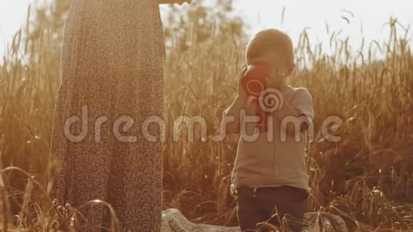 一个可爱的小男孩正从杯子里喝酒妈妈带着一个穿着民族服装的孩子在黑麦场野餐3d视频的预览图