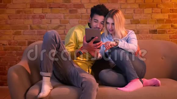 特写镜头非洲男子手持平板电脑和白种人金发女孩在上面打字讨论在家的内容视频的预览图