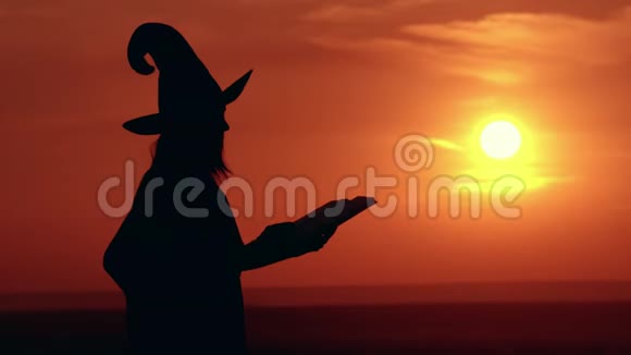 穿着奇装异服的女孩和戴着帽子的女巫魔术手捧大魔法书日出观视频的预览图
