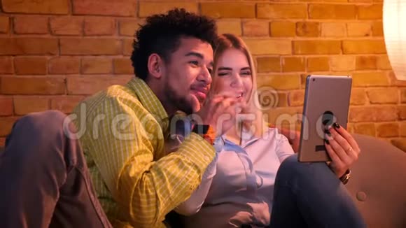 非洲男人和白种人女孩在平板电脑上有一个视频卡在家里既可爱又有趣视频的预览图
