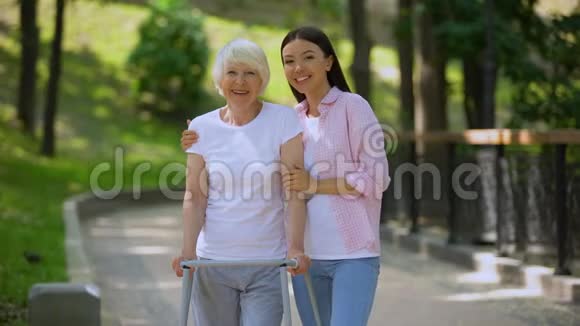 年轻女性拥抱老年妇女带行走架户外康复视频的预览图