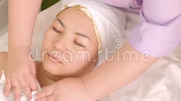 美容师擦拭皮肤从一个亚洲女孩的脖子和脸上的藻类中清洁化妆品面具的遗骸关闭视频的预览图