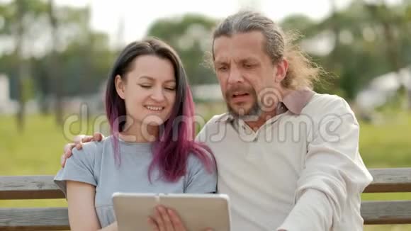 放松迷人的中年男子留着长长的灰色头发一个年轻的女人染着头发拥抱着看着一张照片视频的预览图