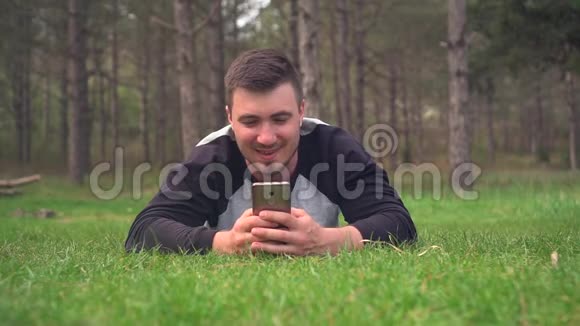 一个年轻人躺在森林里的绿草上看着电话休息放松愉悦视频的预览图