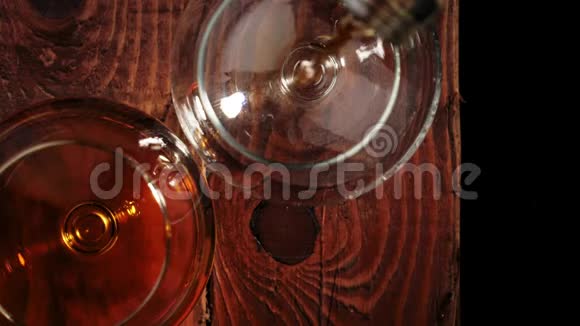 豪华白兰地手把金白兰地从一个圆形的瓶子里倒入一个玻璃杯里放在靠近杯子的棕色木桌上视频的预览图
