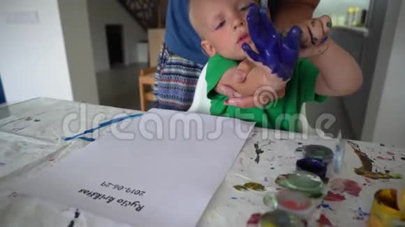 母亲和幼儿儿子用水彩在纸上制作手印邮票视频的预览图