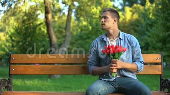担心男人和一群郁金香在公园的长椅上等女朋友约会视频的预览图