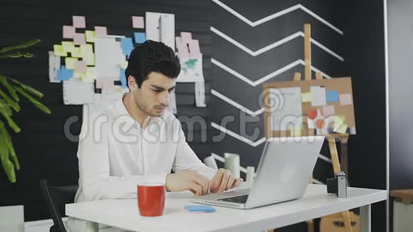 昏昏欲睡的疲惫的年轻人坐在办公室桌面上手提电脑视频的预览图