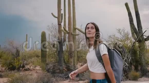 慢动作美丽的年轻微笑的旅游妇女徒步沿着炎热的仙人掌沙漠国家公园在暴风雨的夏季天空视频的预览图
