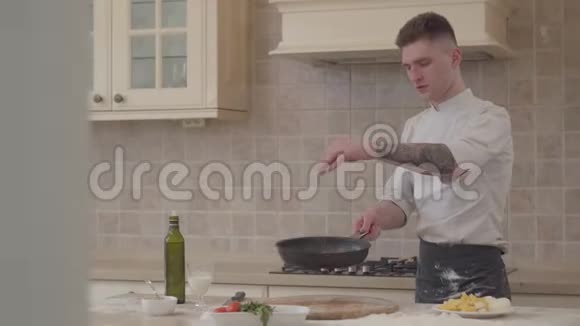 穿厨师制服的年轻人把盐放进煎锅里把肉扔进煎锅里专业厨师倒牛奶视频的预览图