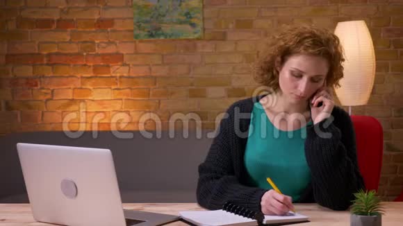 一位成年女商人在办公室里用手提电脑打字打电话记笔记的特写镜头视频的预览图
