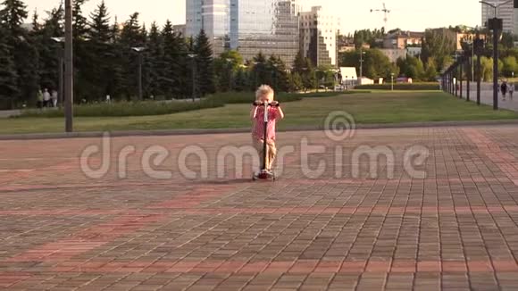 日落时分一个穿着红色格子衬衫的小男孩在城市公园骑滑板车视频的预览图