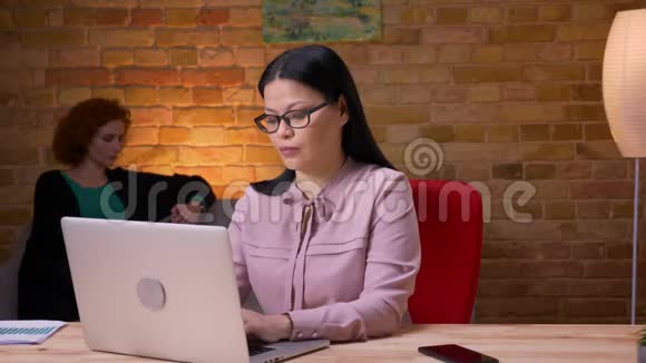 在笔记本电脑上工作的成年亚洲女商人收到电话通知的特写镜头微笑着视频的预览图