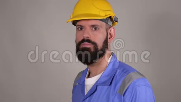 戴头盔的胡子男工人敬礼手在灰色背景上挥舞视频的预览图