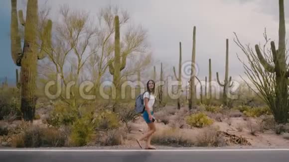 慢动作宽镜头快乐的年轻成年旅游妇女走在惊人的野生仙人掌沙漠路在国家公园视频的预览图
