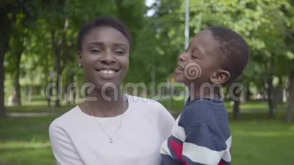 肖像可爱的非洲裔美国妇女抱着她有趣的儿子在她的怀里在绿色公园近距离爱的家庭视频的预览图