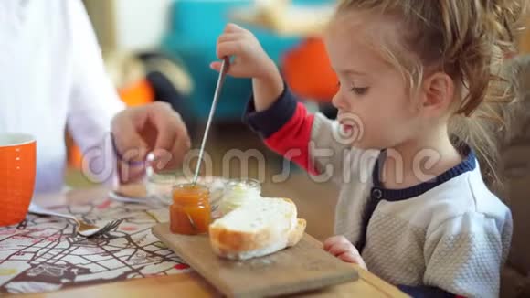 小白种人女孩孩子和母亲在咖啡馆的一张桌子上吃美味的面包和果酱视频的预览图
