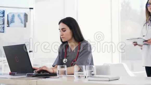 年轻的一群医生在医院开会时使用笔记本电脑纸质文件多民族小组视频的预览图