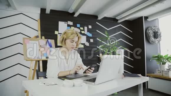 拥有智能手机的漂亮女设计师坐在办公室里视频的预览图