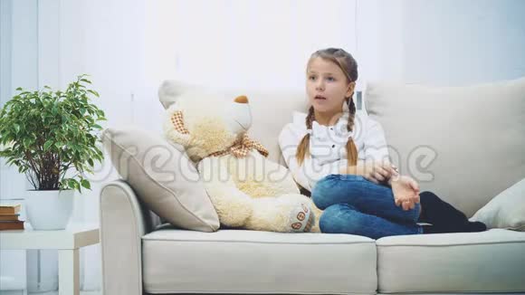 可爱的小女孩坐在沙发上和她的泰迪说话拼命地弯曲她的手指视频的预览图