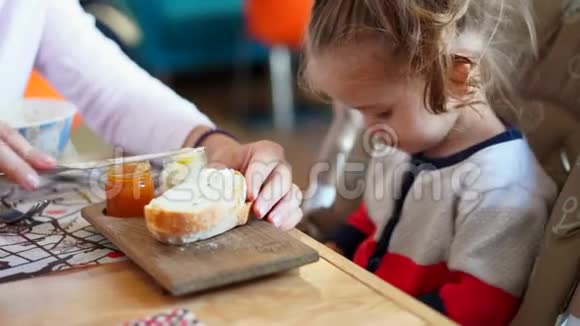 小白种人女孩孩子和母亲在咖啡馆的一张桌子上吃美味的面包和果酱视频的预览图
