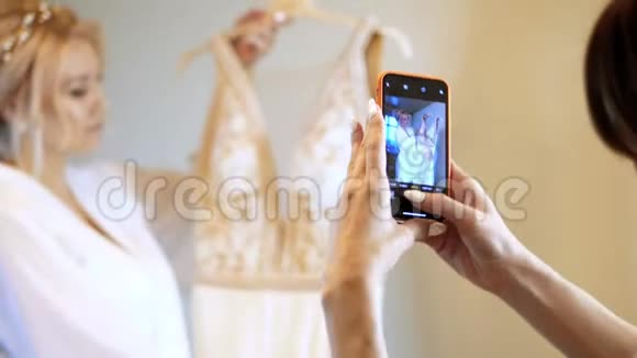 一位穿着白色长袍的新娘手里拿着一个衣架手里拿着一件婚纱检查它特写女性双手视频的预览图
