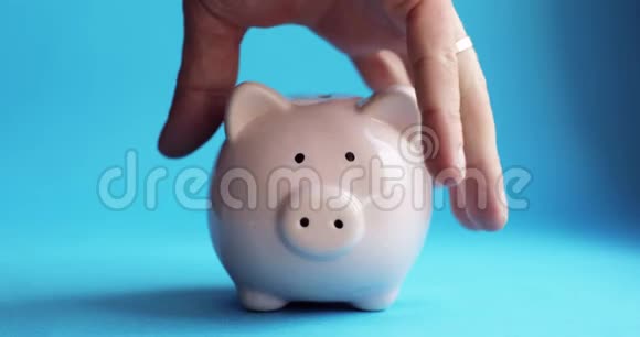 人摇动猪形的储蓄罐硬币在蓝色的背景下从里面掉出来视频的预览图