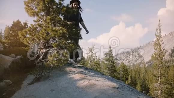 镜头倾斜着快乐美丽的旅游女孩的腿在大石头上徒步旅行探索约塞米蒂国家公园的慢动作视频的预览图