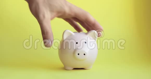 人摇动猪形的储蓄罐硬币掉在黄色的背景上视频的预览图