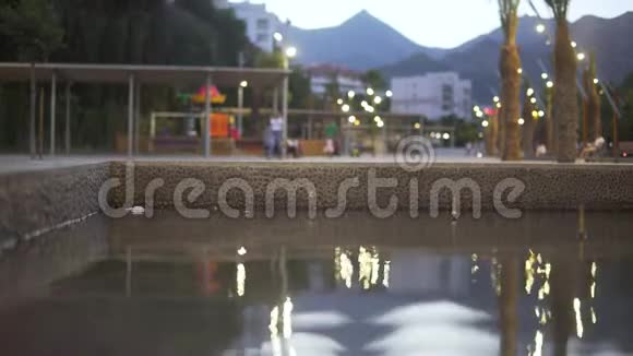 游泳池在步行公园背景是山晚上人们在公园里散步视频的预览图